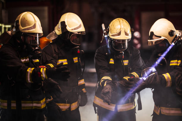 istock Group of professional firefighters. Firemen wearing uniforms, protective helmets and oxygen masks. Smoke in the background. 1341136105