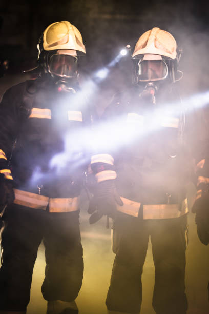 istock Group of professional firefighters. Firemen wearing uniforms, protective helmets and oxygen masks. Smoke in the background. 1341136134