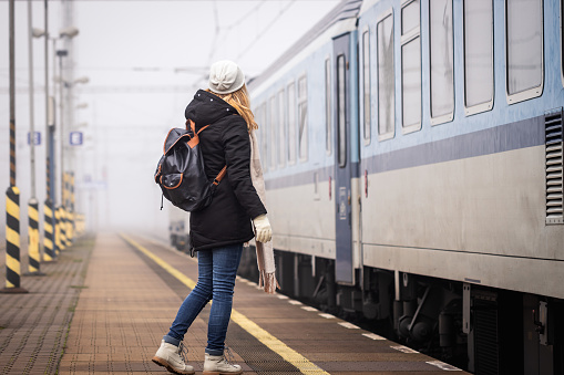 Woman with backpack boarding to train at railroad station in foggy morning. Railway transportation