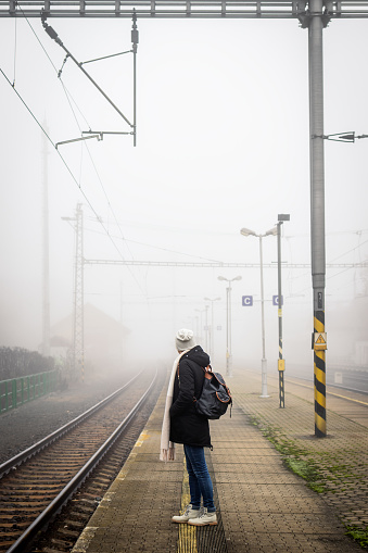 Solo female traveler waiting for train on empty foggy railroad station platform