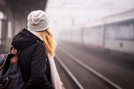 Travel by train. Woman waiting for train on foggy railway station. Female tourist standing at railroad platform