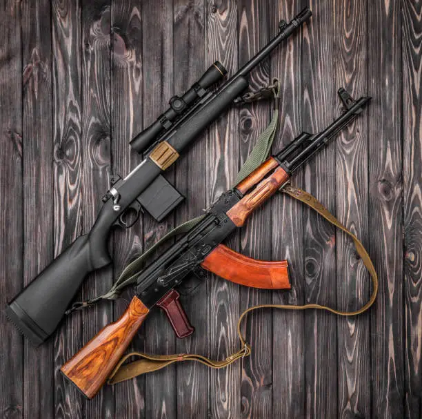 Photo of Two weapons lie on a plank surface. An old Soviet automatic carbine and a modern bolt-action rifle with a telescopic sight. Weapon on a wooden background.