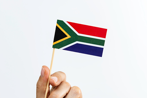 Hand is holding flag of South Africa on white background.