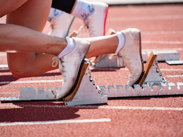 view of female feet on starting block ready for a sprint start Side view of female feet on starting block ready for a sprint start. Naked female legs in light running shoes. World Athletics Day stock pictures, royalty-free photos & images
