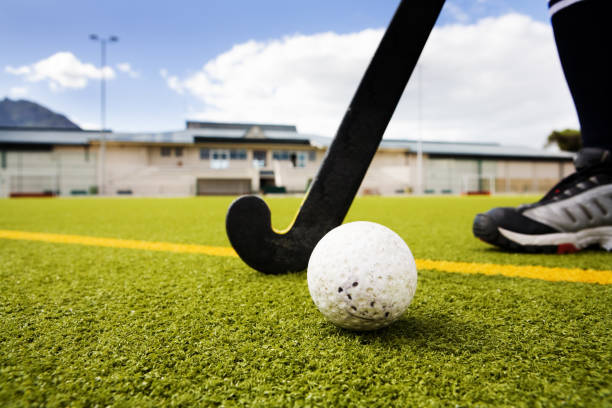 Hockey Hockey player, stick and ball on artificial turf. Pavilion and floodlight in the background. field hockey stock pictures, royalty-free photos & images