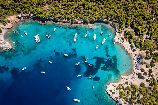 Aerial top down view of the many boats moored at the popular beach of Moni island, Aegina, Saronic Gulf, Greece with turquoise sea and lush, green hills