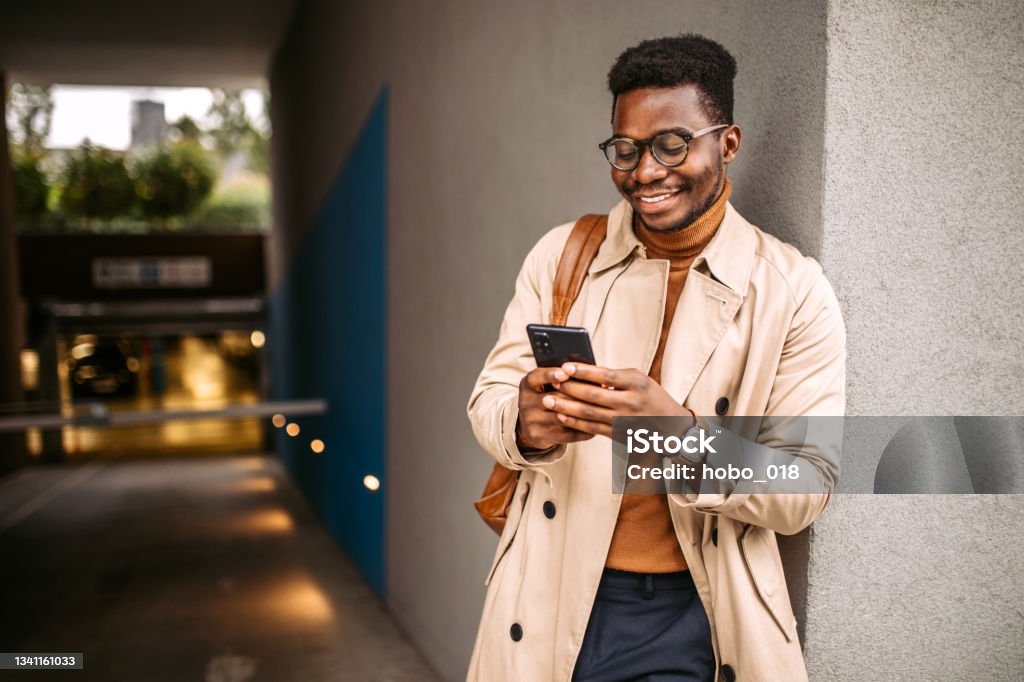 Businessman waiting for a ride to the work Young handsome black businessman waiting for an uber, using mobile phone for communication. Using Phone Stock Photo