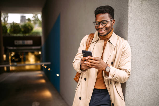 Businessman waiting for a ride to the work Young handsome black businessman waiting for an uber, using mobile phone for communication. urbane stock pictures, royalty-free photos & images