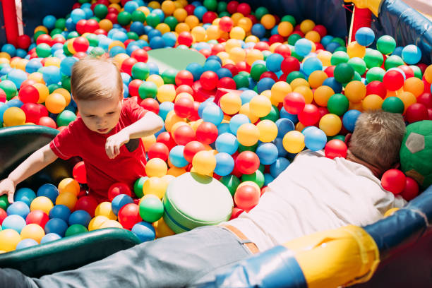 Happy laughing boy 1-2 years old having fun in ball pit on birthday party in kids amusement park and indoor play center. Child playing with colorful balls in playground ball pool. Activity toys for little kid. feliz niño risueño de 1-2 años divirtiéndose con su abuelo en el pozo de bolas en la fiesta de cumpleaños en el parque de diversiones para niños y el centro de juegos cubierto. niño jugando con pelotas de colores en la piscina de bolas del patio de