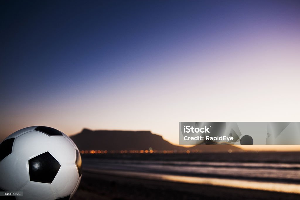 Soccer ball against silhouetted Table Mountain Championship soccer ball sits on the beach overlooking Cape Town and Table Mountain as night falls. South Africa hosts the 2010 World Cup. Focus is on the ball. Shot with Canon EOS 1Ds Mark III.  2010 Stock Photo