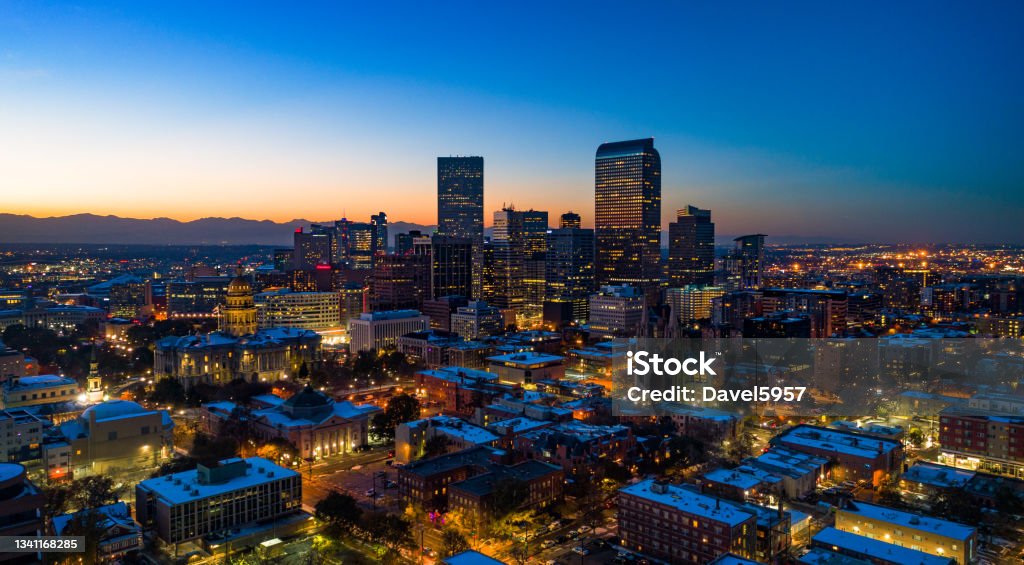 Denver Skyline Aerial At Dusk With Sunset And Mountains Downtown Denver skyline aerial at dusk with the sunset and Rocky Mountains in the far background, the metropolitan area in the background, and various buildings in the foreground including the Colorado State Capitol building in the left. Denver Stock Photo