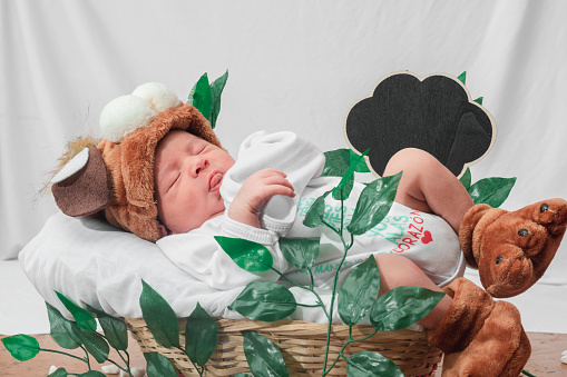 Beautiful newborn baby (4 days old), with hat and puppy shoes, in bamboo fiber basket and surrounded by green leaves, Healthy medical concept