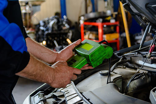 Photo of an Experienced Car Mechanic who is Checking the Car Battery with Electric Tools.