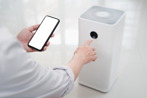 Close up hand a man holding smartphone with white screen display and online connect to air purifier using technology to control health equipment anywhere via the Internet