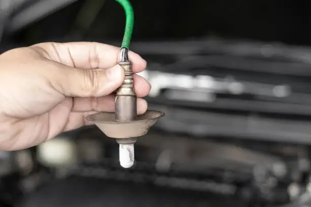 Photo of Close up hand car mechanic hold oxygen sensor of exhaust system of gasoline engine checking for faults in the exhaust system in the maintenance of the vehicle that has been used for a long time
