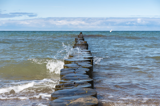 Water from the baltic sea splashing against a row of wooden planks. A wave moves towards the beach. Fresh water drops are flying through in the air.