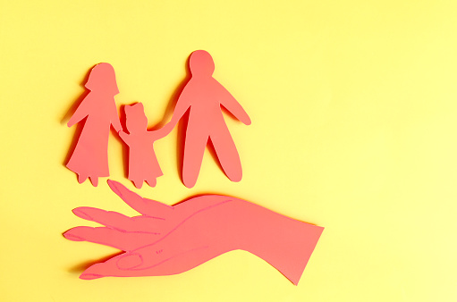 A cardboard hand holding a family with a child on a colored background. The concept of family relations adults and children copy the space