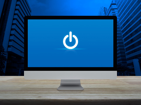 Power button icon on desktop modern computer monitor screen on wooden table over office city tower and skyscraper, Business start up online concept
