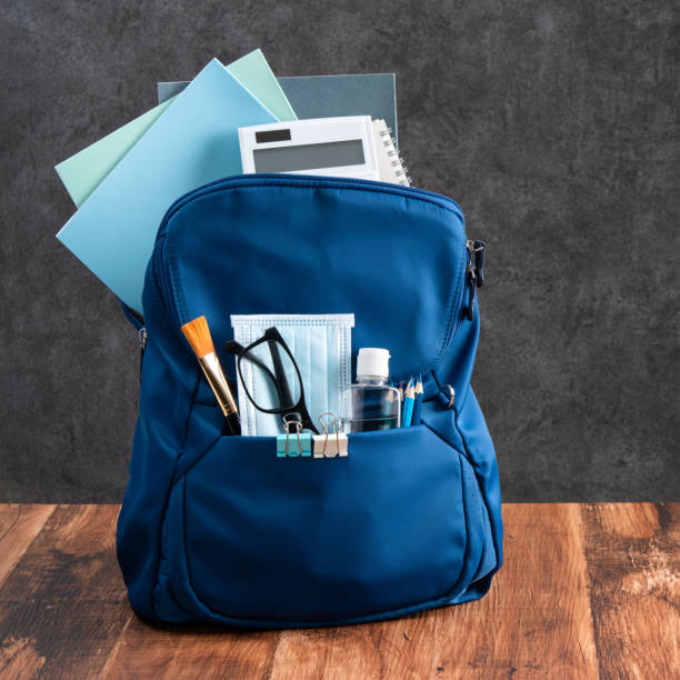 istock Blue backpack with stationery over wooden table and black background. 1341212161
