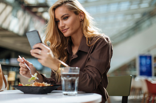 Beautiful woman using phone during lunch in food court
