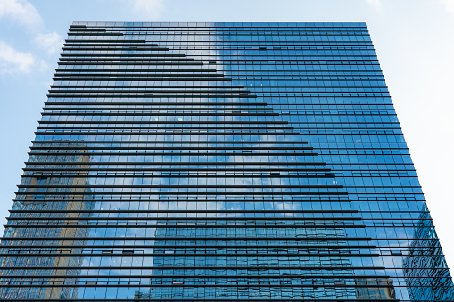 Bottom view of modern architecture. Blue sky and white clouds are reflected on the glass outer wall