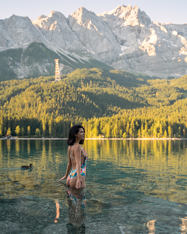 Young happy woman in swimsuit alone slowly going to swim in lake