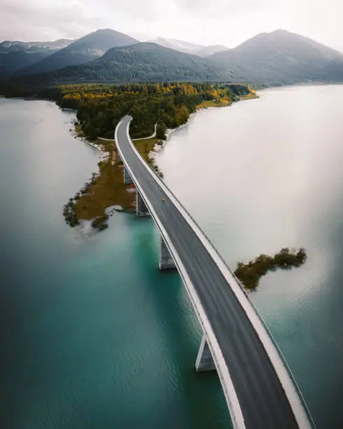 Aerial view, taken by drone, of a man walking alone in the middle of a urban bridge, surrounded by lake during the day.