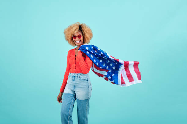 istock Young woman smiling while holding a US flag on an isolated background. 1341221306