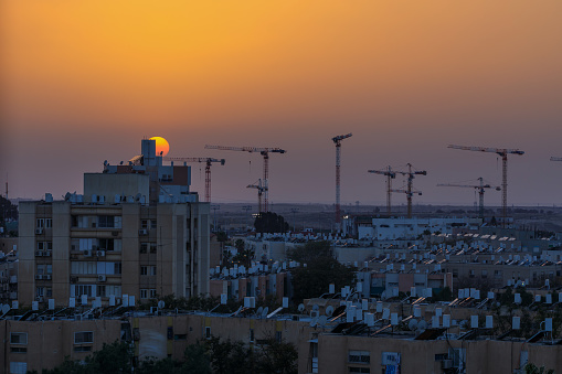 Sun move down behind the building and many cranes who is build new residential district in Beer-Sheba, Israel