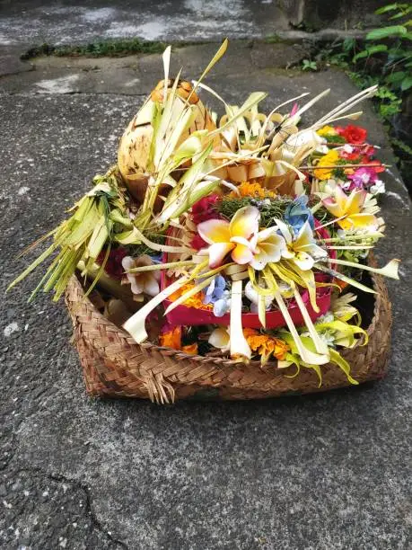 Photo of Handwoven basket piled high with colorful traditional floral prayer offerings on the sidewalk in Bali Indonesia