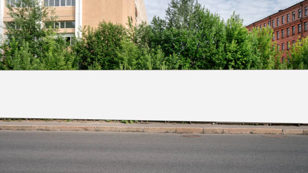 Long huge hoarding with empty space for mockup on street pavement. Long huge hoarding with empty space for mockup on street pavement. Industrial and business promotion concept. greed stock pictures, royalty-free photos & images