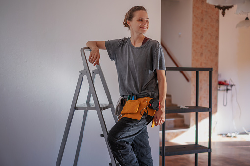 Beautiful woman repairman standing on stepladder making repairs at home