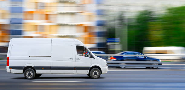 la furgoneta blanca conduce sobre el tráfico de la ciudad en el fondo del paisaje urbano. - mini van fotografías e imágenes de stock