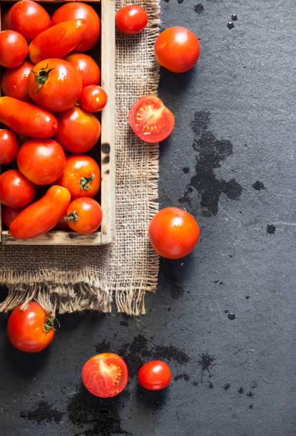 istock Fresh red tomatoes in wooden box on black background 1341235802