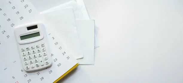 Photo of close up top view on calculator and calendar over group of invoice letter mail from bank on white background for money and debt  management concept