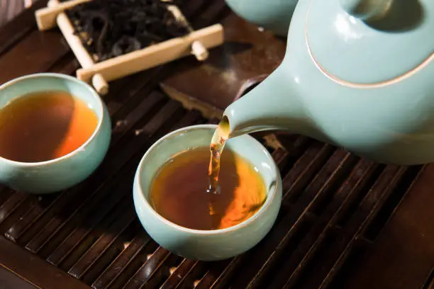 Photo of black tea in a teapot is poured into cups.