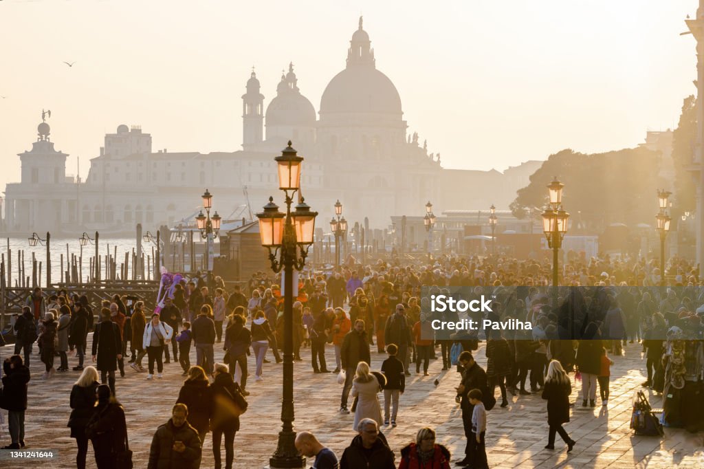Crowd of tourists at the carnival in St. Mark's Square, in the background the Basilica of Santa Maria della Salute,Venice, Italy, Europe Crowd of tourists at the carnival in St. Mark's Square, in the background the Basilica of Santa Maria della Salute,Venice, Italy, Europe,Grand Canal and Basilica Santa Maria della Salute in Venice, Italy. Famous tourist destination Ancient Stock Photo