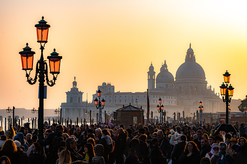 Crowd of tourists at the carnival in St. Mark's Square, in the background the Basilica of Santa Maria della Salute,Venice, Italy, Europe,Grand Canal and Basilica Santa Maria della Salute in Venice, Italy. Famous tourist destination