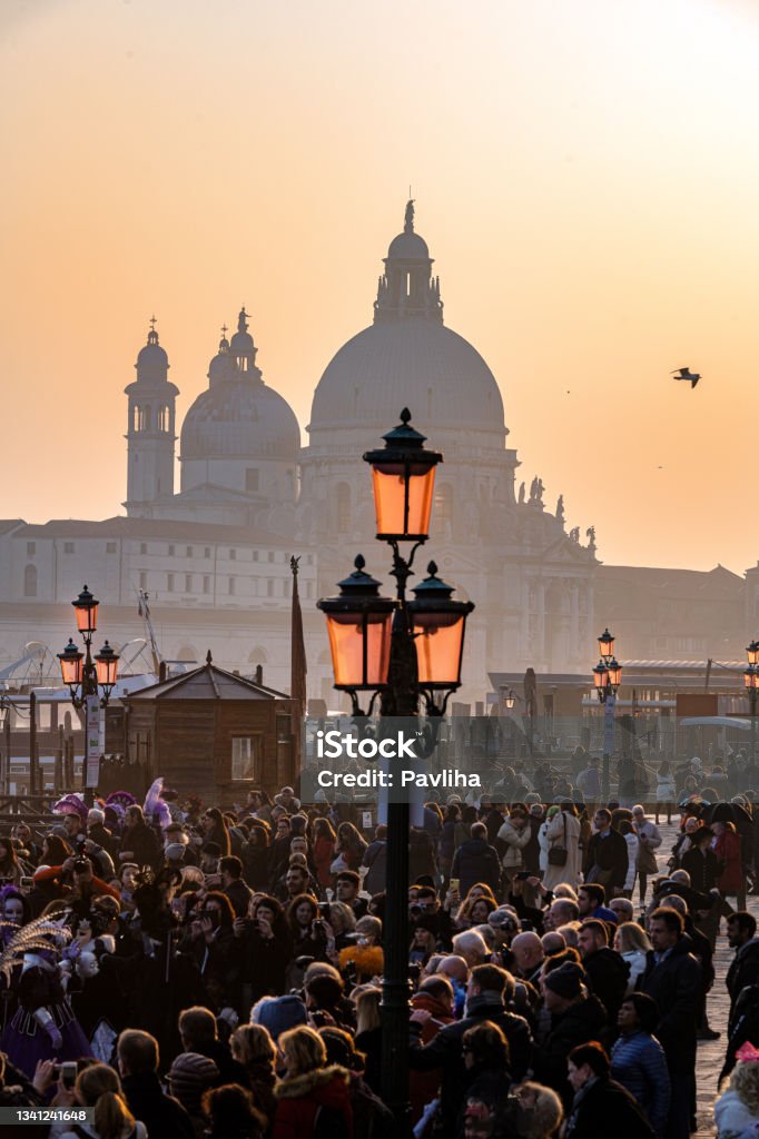 Crowd of tourists at the carnival in St. Mark's Square, in the background the Basilica of Santa Maria della Salute,Venice, Italy, Europe Crowd of tourists at the carnival in St. Mark's Square, in the background the Basilica of Santa Maria della Salute,Venice, Italy, Europe,Grand Canal and Basilica Santa Maria della Salute in Venice, Italy. Famous tourist destination Crowd of People Stock Photo