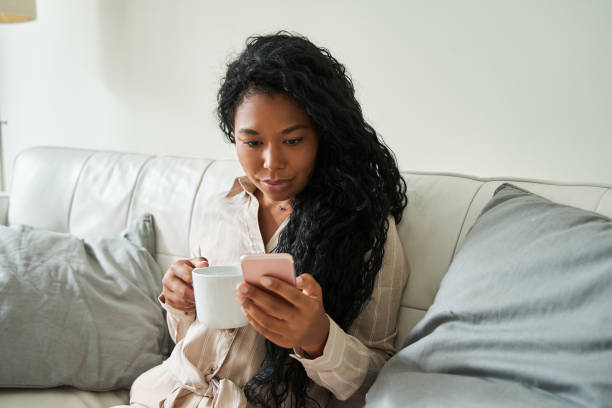 istock Woman drinking coffee and looking at her smartphone while spending time at home 1341245663