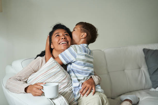 Black boy hugging his happy mother on couch stock photo