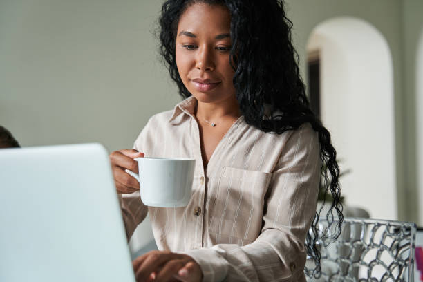 istock Woman drinking coffee and looking at her laptop computer while working at home 1341245672