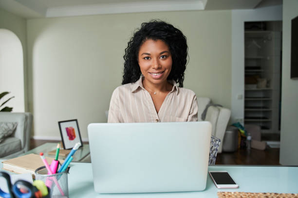 istock Woman sitting at the table and typing at her laptop computer while smiling to the camera 1341245688
