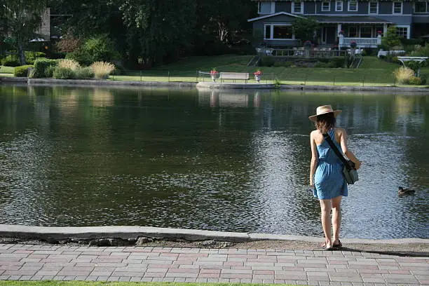 A girl walks down to the water's edge to see the ducks.