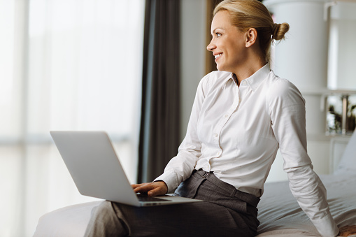 Businesswoman looking through window while using laptop in a hotel room