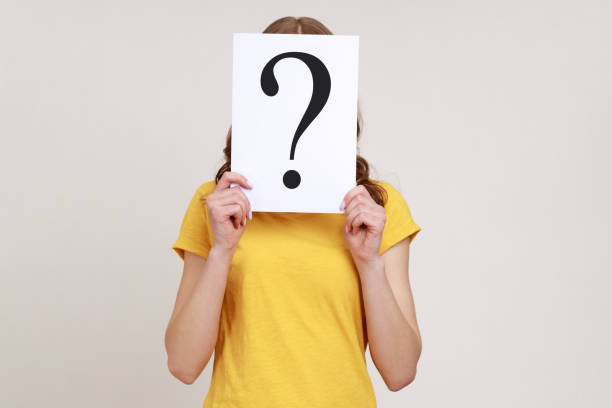 portrait of shy woman in yellow casual t-shirt, hiding her face behind white paper with question mark, finding smart solution, asking for advice. - pensive question mark teenager adversity imagens e fotografias de stock