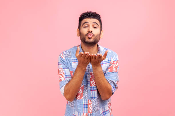 ¡atrapa mi beso de amor! retrato de un joven adulto barbudo con camisa azul besando aire sobre las palmas, demostrando sentimientos románticos, afecto. - blowing men kissing blowing a kiss fotografías e imágenes de stock