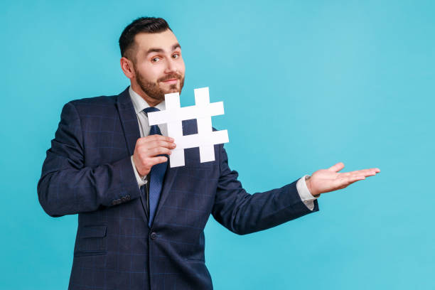istock Man wearing official style suit, holding white hashtag and presenting at copy space on her palm, empty place for idea presentation, product advertising. 1341255458