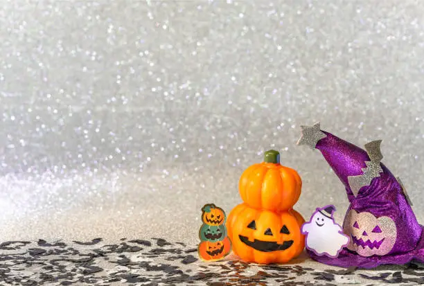 Photo of Halloween jack o lantern pumpkin and witches hat with smiling ghost  on  a glitter silver background.