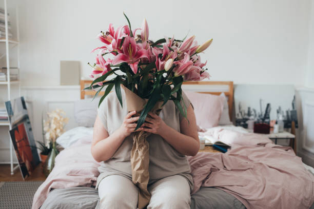 mulher plus size sentada na cama e segurando flores - beautiful white pink messy - fotografias e filmes do acervo